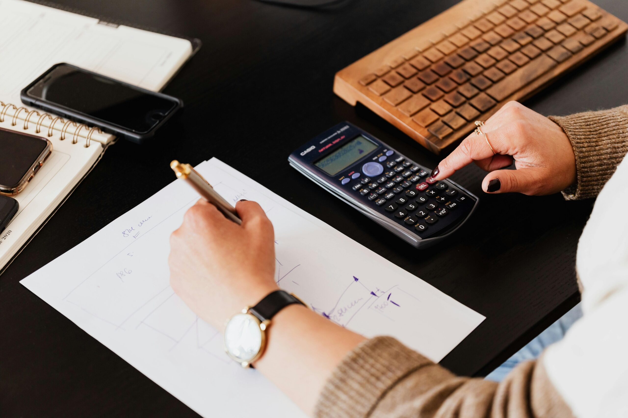 pexels-photo-4476375-4476375 Close-up of hands working with a calculator and notebook on a desk, analyzing documents.